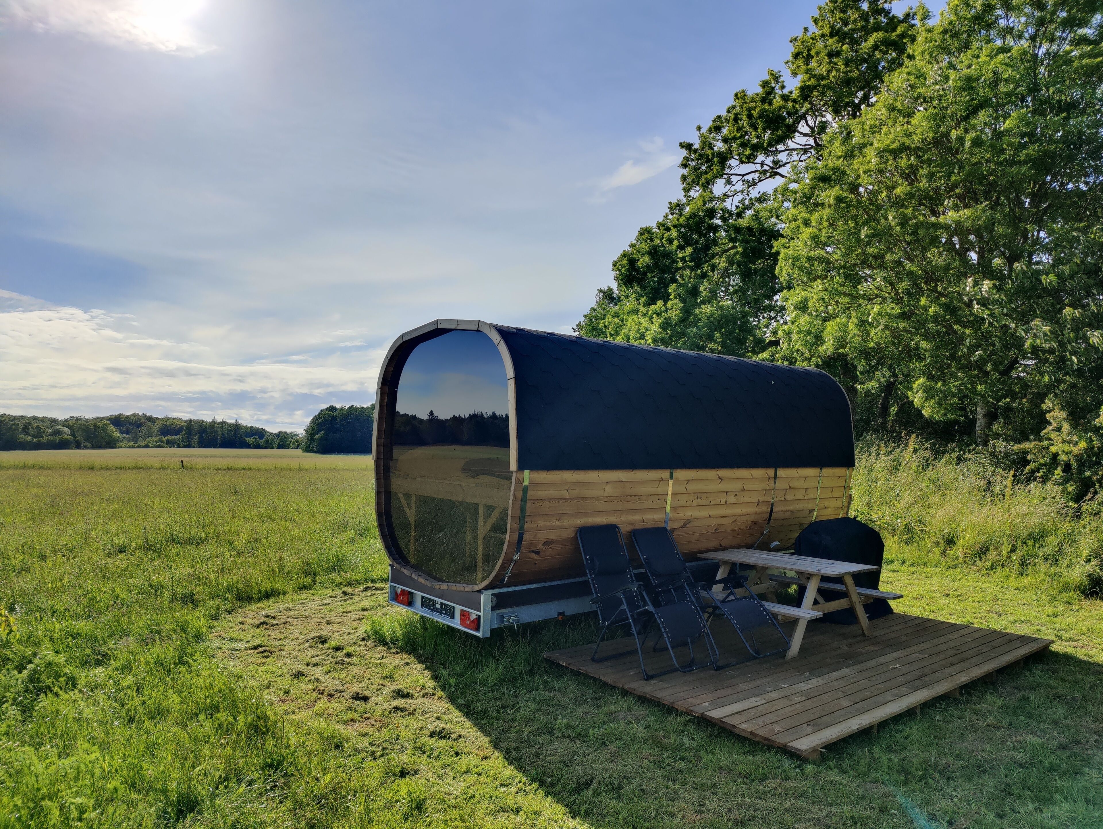 A covered RV with a wooden exterior, a picnic table, and four chairs in a grassy field.