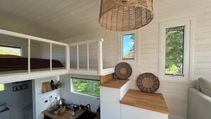 A compact kitchen with a wooden countertop, a sink, and a hanging woven light fixture. - Under Canvas Bornholm (Østermarie)