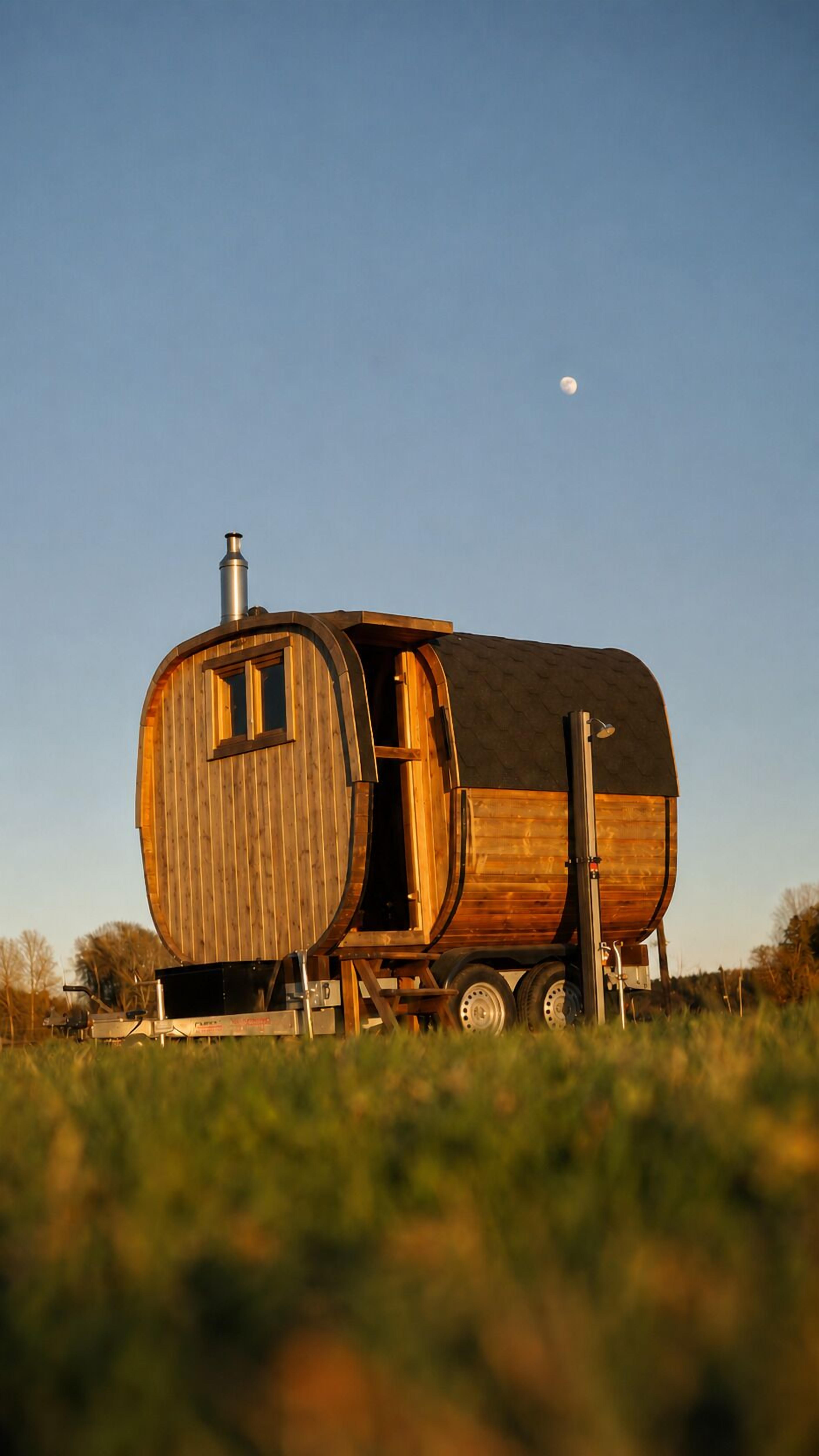 Une structure cylindrique en bois, dotée d’une cheminée, de roues et d’une petite fenêtre.