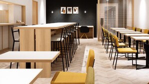 Un comedor moderno con varias mesas y sillas, una pared de acento negra con obras de arte enmarcadas y un ventanal con persianas.