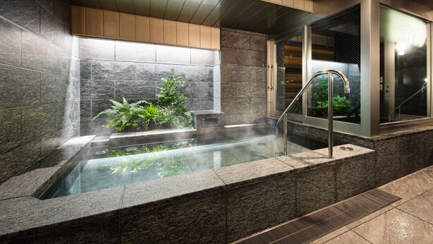 Un espacio de spa moderno con un jacuzzi, ducha con cerramiento de vidrio y una pared vegetal.