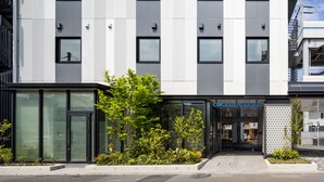 Un hotel moderno con fachada limpia y geométrica, ventanas amplias y un área de entrada bien cuidada con plantas.