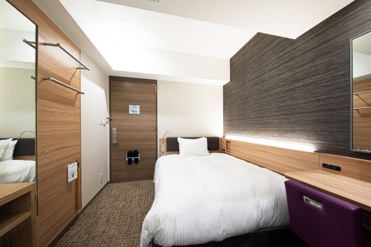 Une chambre d’hôtel comprenant un lit, une armoire, un miroir et un porte-chaussures.