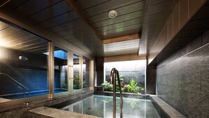 Un área de piscina interior moderna con cerramiento de vidrio, una escalera de metal y vistas al exterior.