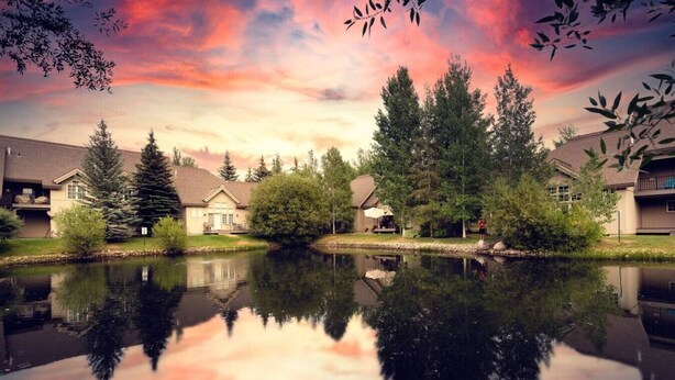 Una vista tranquila de un lago con casas, árboles y un reflejo claro en el agua.