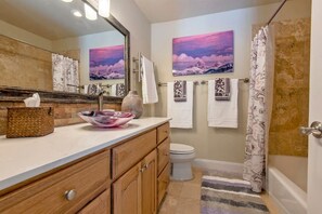 Un baño con tocador de madera, un espejo grande, un lavabo, dos toallas, una cortina de ducha y dos cuadros colgados en la pared.