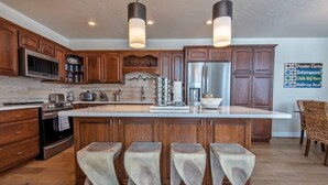 A modern kitchen with wooden cabinets, stainless steel appliances, and a central island with bar stools. - Aspen Pointe Glass House on Ski Hill Road Driggs, ID (Driggs)