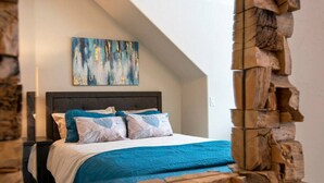 A bedroom with a bed, a headboard, a painting on the wall, and a wooden wall feature. - Aspen Pointe Glass House on Ski Hill Road Driggs, ID (Driggs)