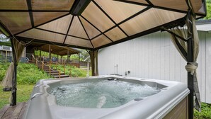 A hot tub under a covered patio with a wooden deck and a white fence in the background. - Family Retreat, outdoor oasis, game room (Broken Bow)