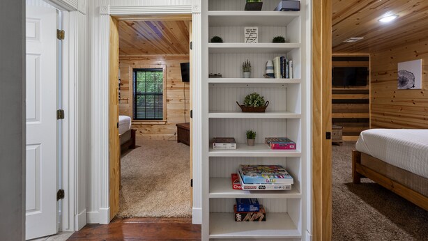 A room with a wooden floor, a white door, a bookshelf, a bed, and a window with blinds. - Family Retreat, outdoor oasis, game room (Broken Bow)