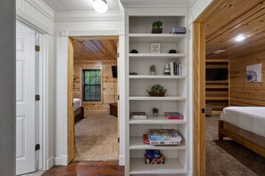 A room with a wooden floor, a white door, a bookshelf, a bed, and a window with blinds. - Family Retreat, outdoor oasis, game room (Broken Bow)