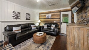 A living room with a black leather sectional sofa, a round ottoman, and a wooden cabinet. - Family Retreat, outdoor oasis, game room (Broken Bow)
