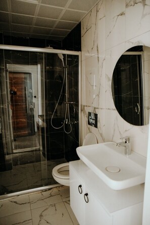 A modern bathroom with a glass-enclosed shower, a toilet, and a sink with a mirror. - Soral Apart Otel (Demre)
