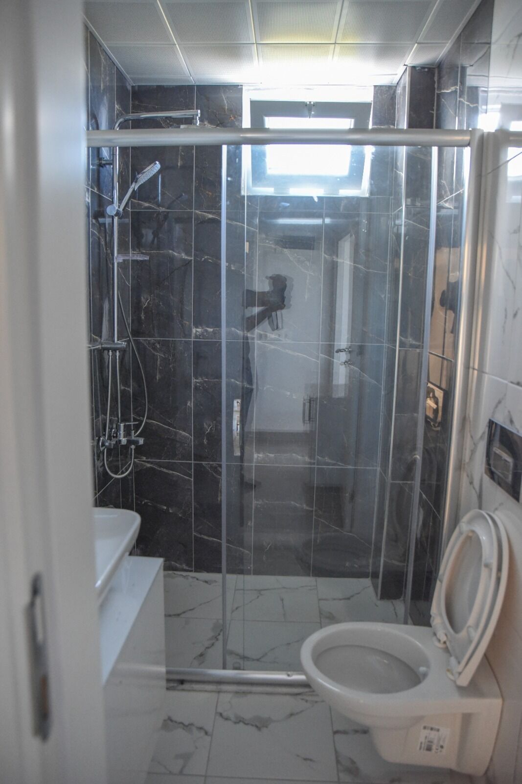 Un baño con cabina de ducha de vidrio, inodoro y lavamanos.