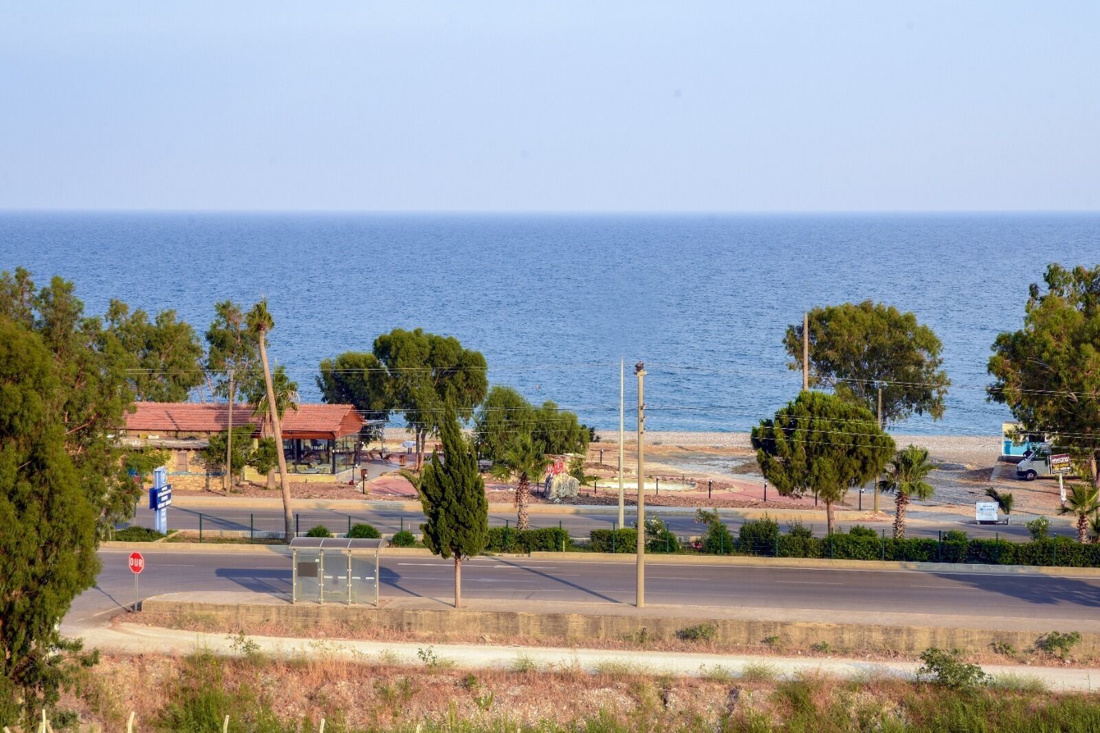 Una carretera costanera amb una vista despejada del mar, una àrea de pàrquing i un edifici amb teulada vermella.