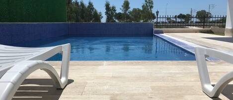 A swimming pool with a tiled edge and a green hedge.