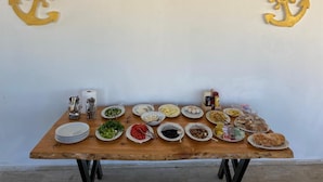 A wooden table with various dishes and condiments, set against a plain wall with two golden anchors. - Soral Apart Otel (Demre)