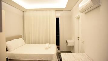 Una habitación de hotel con cama, mesita de noche, una pequeña mesa, armario y aire acondicionado.