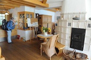Une pièce avec un plancher en bois, une table à manger avec des chaises, un fauteuil en osier, une cheminée et une personne debout près d’un tableau d’affichage.