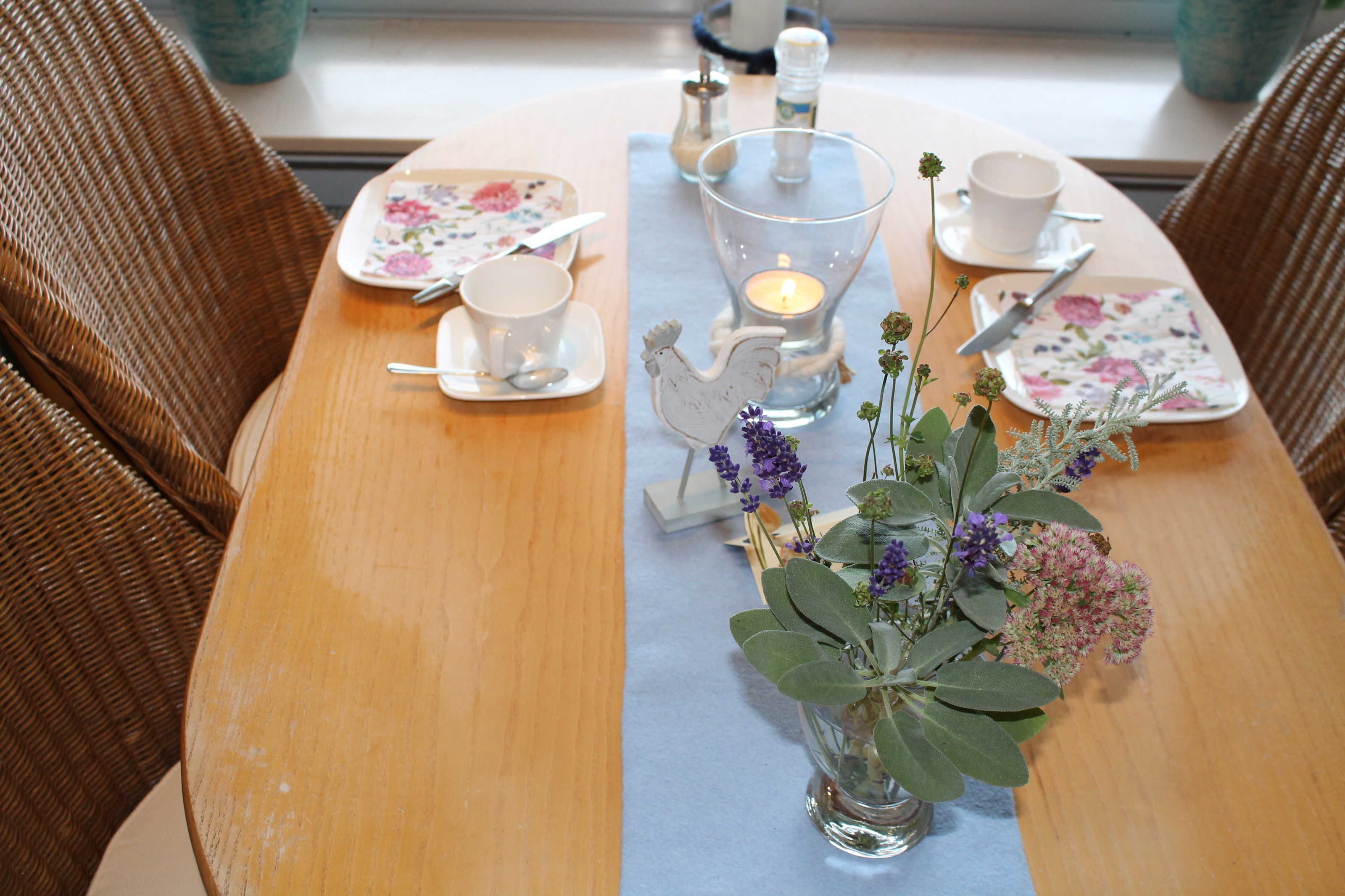 A dining table with floral tableware, a candle, and a vase with flowers.