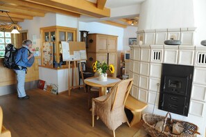 Ein Zimmer mit Holzboden, einem Esstisch mit Stühlen, einem Korbstuhl, einem Kamin und einer Person in der Nähe eines Schwarmsbretts.