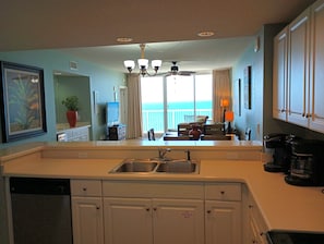 A kitchen with a built-in sink, a ceiling fan, and a view of the ocean through large windows.