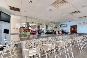 A bar area with a tiled backsplash, metal chairs, and a variety of liquor bottles.