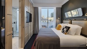 Ett modernt hotellrum med en stor säng, en TV, en balkong med utsikt över staden och en dusch.