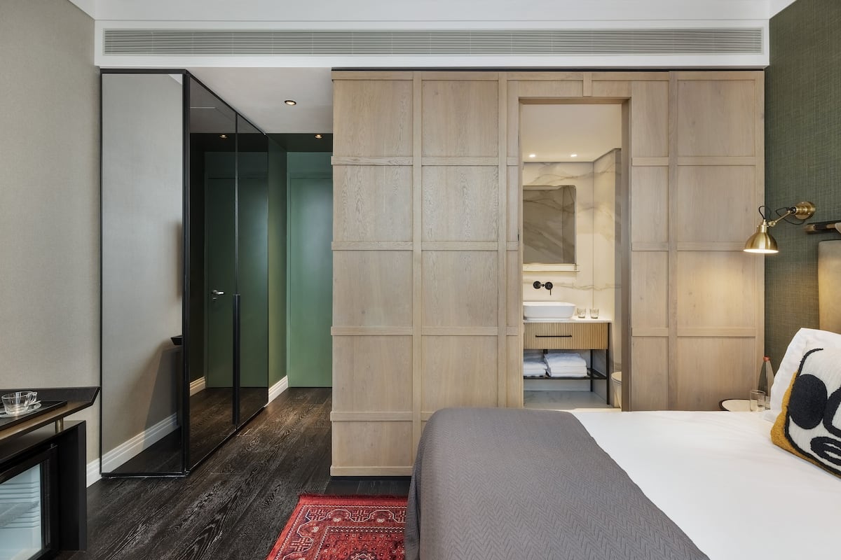 A modern hotel room with a large bed, a walk-in closet, a glass shower, and a small bedside table.