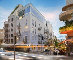 A modern hotel with multiple balconies, a prominent entrance, and a street view with outdoor seating.