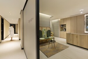 Una hall d'albergo moderna con una reception, un'area salotto e una persona che cammina lungo il corridoio.