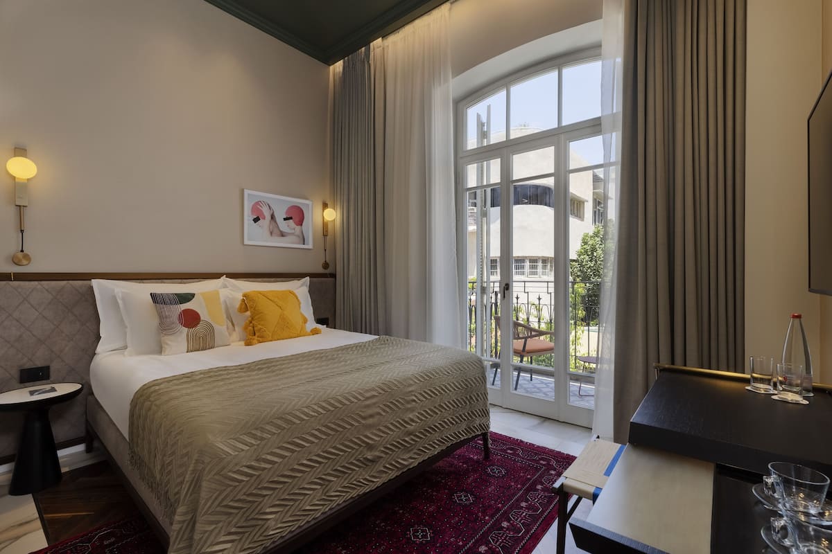 A hotel room with a bed, a desk, a chair, a small table, and a large window.