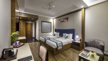 A hotel room with a large bed, a desk, a chair, a small table, a nightstand, and a ceiling fan.