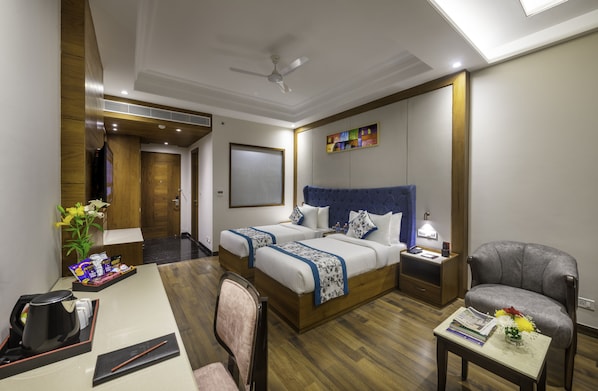 Habitación de hotel con una cama grande, un escritorio, una silla, una mesita pequeña, una mesita de noche y un ventilador de techo.