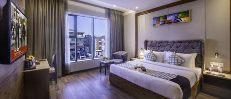 Une chambre d’hôtel moderne dotée d’un grand lit, d’un bureau, d’une chaise et offrant une vue sur la ville grâce à de grandes fenêtres.