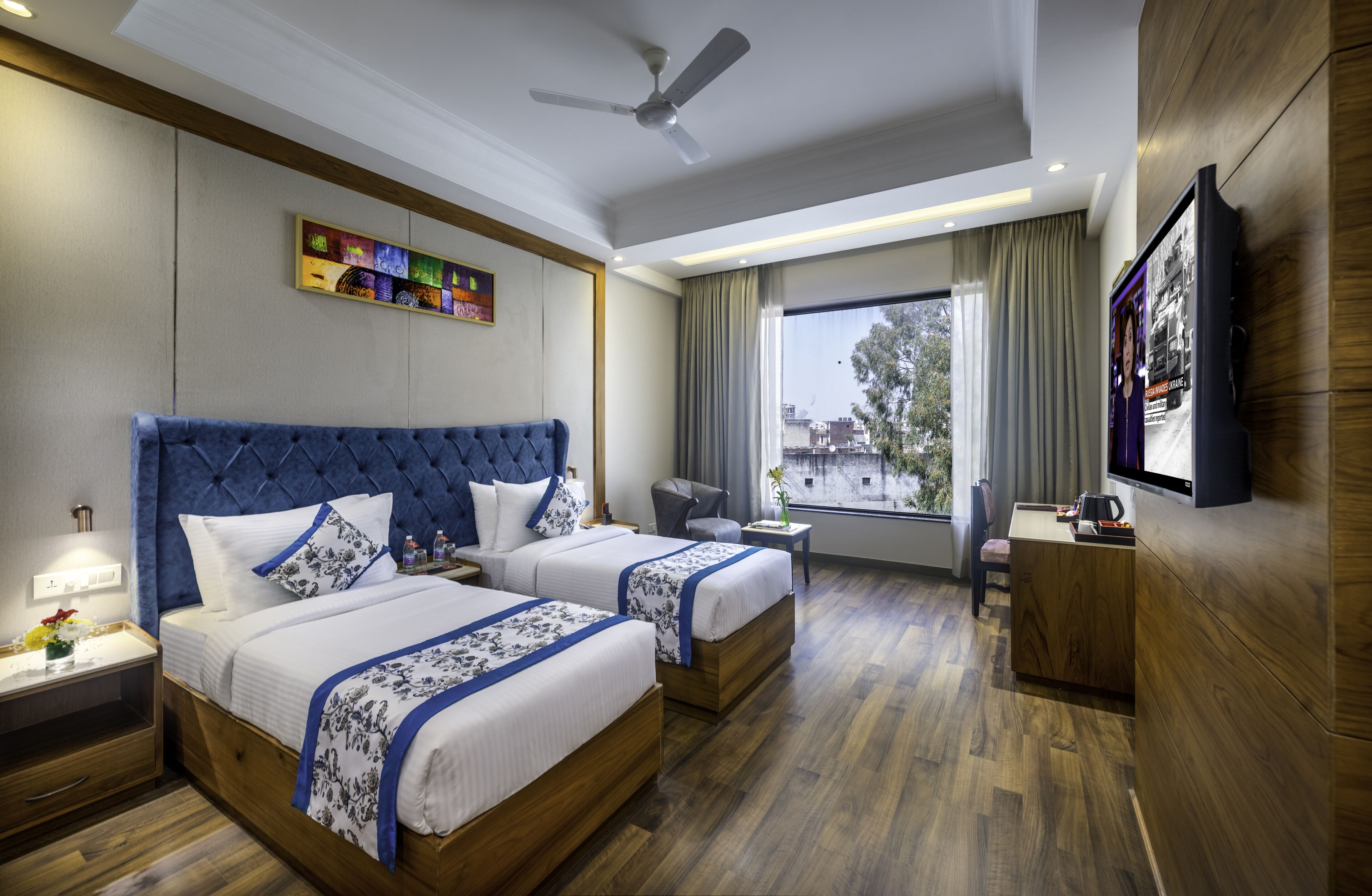 A hotel room with two beds, a desk, a chair, a TV, and a window with a view.