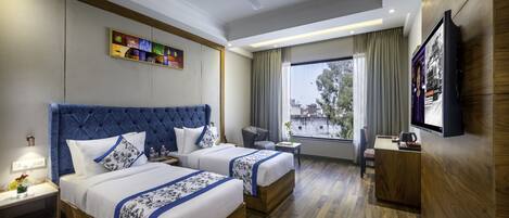 A hotel room with two beds, a desk, a chair, a TV, and a window with a view.