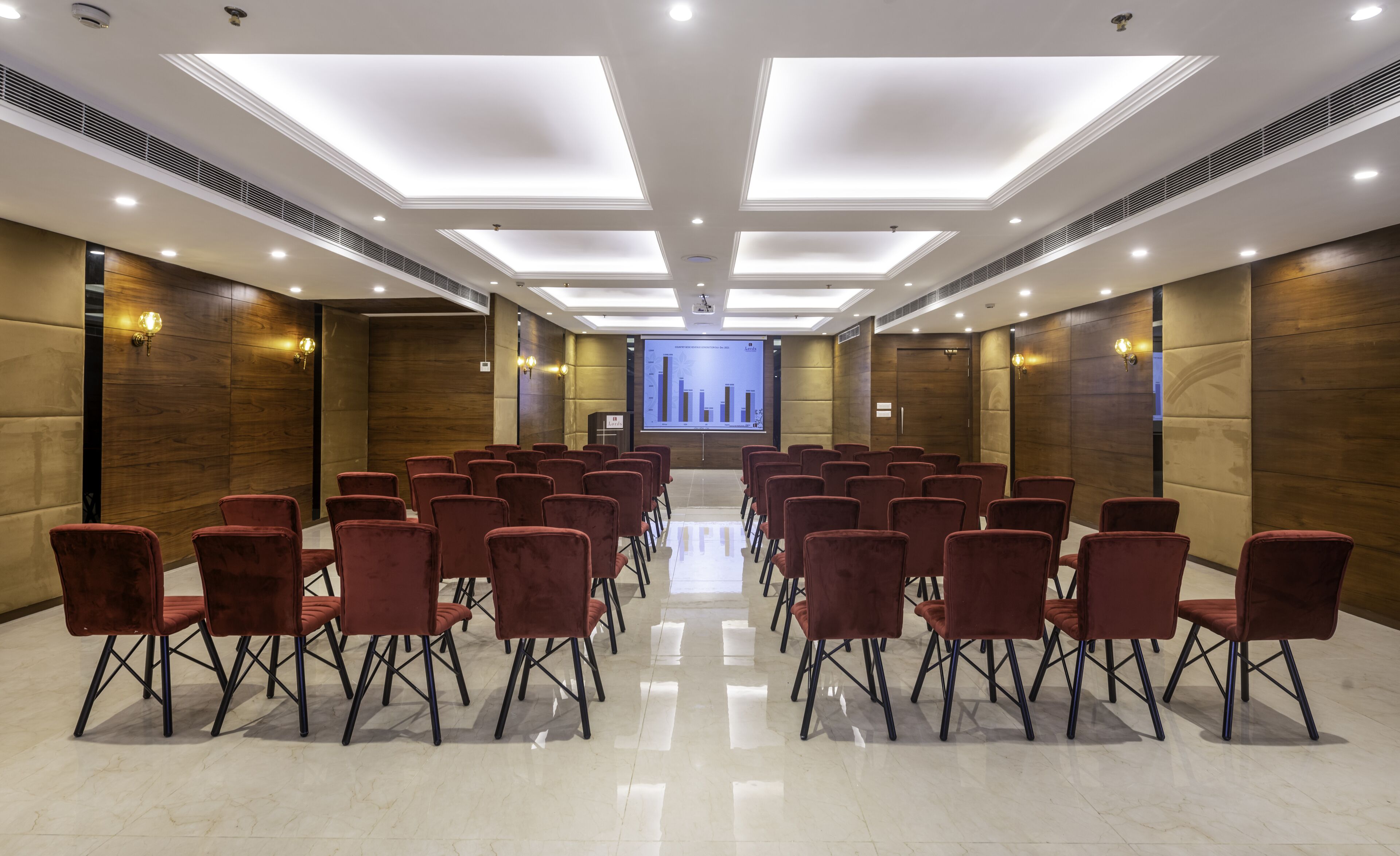 A conference room with rows of red chairs, a large screen at the front, and a modern ceiling design.
