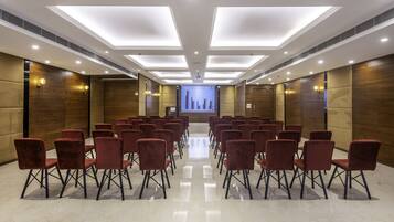 A conference room with rows of red chairs, a large screen at the front, and a modern ceiling design.