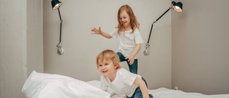 Un enfant saute sur un lit recouvert de draps blancs, dans une pièce où sont fixées deux lampes aux murs.