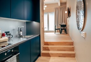 Una cocina moderna con armarios azul oscuro, un lavamanos de acero inoxidable y una escalera de madera que lleva a un comedor con una mesa y sillas.