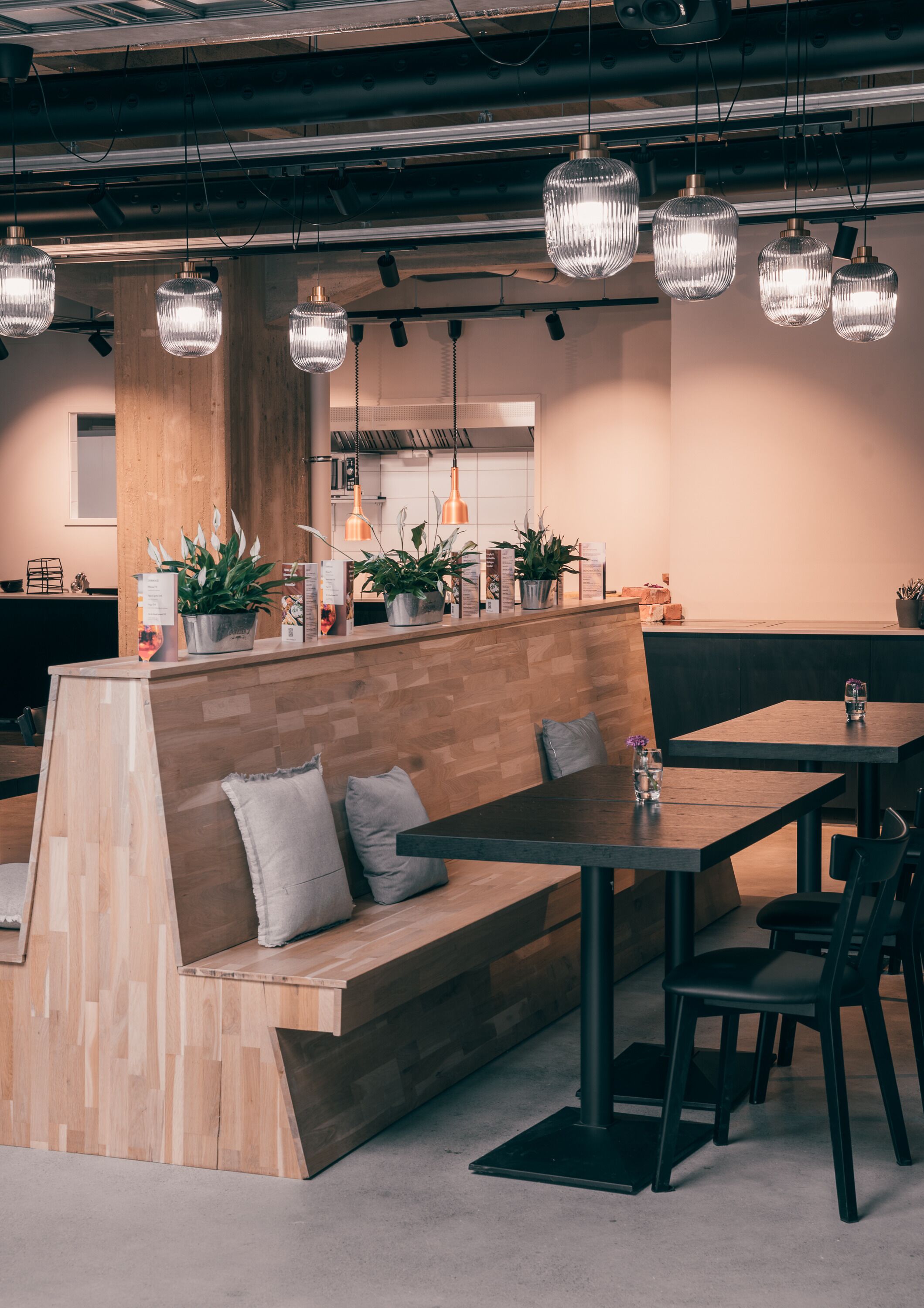 A modern cafe with wooden seating, pendant lighting, and potted plants.
