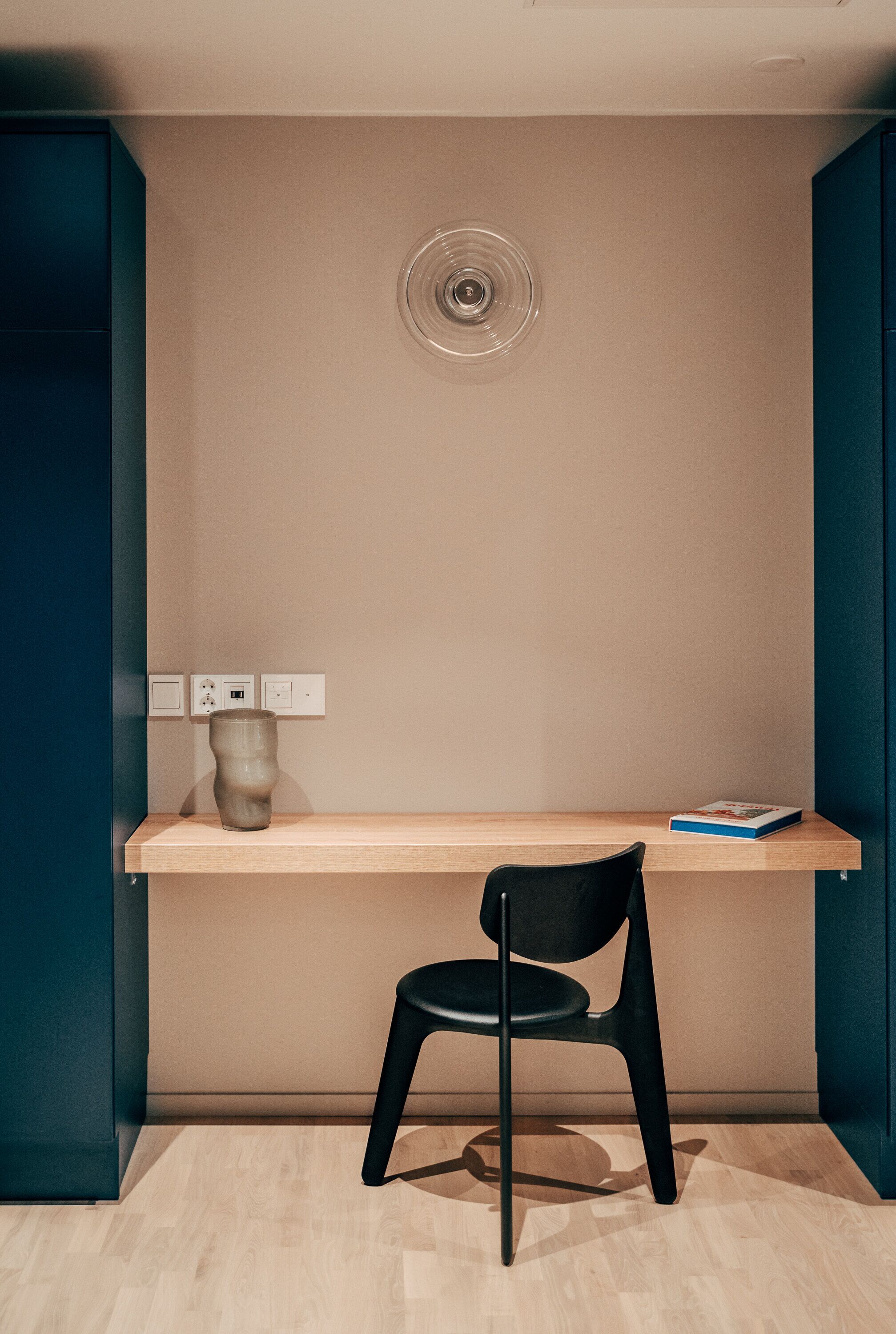 Ein modernes Zimmer mit einem Holztisch, einem schwarzen Stuhl, einer Vase und einem Buch.