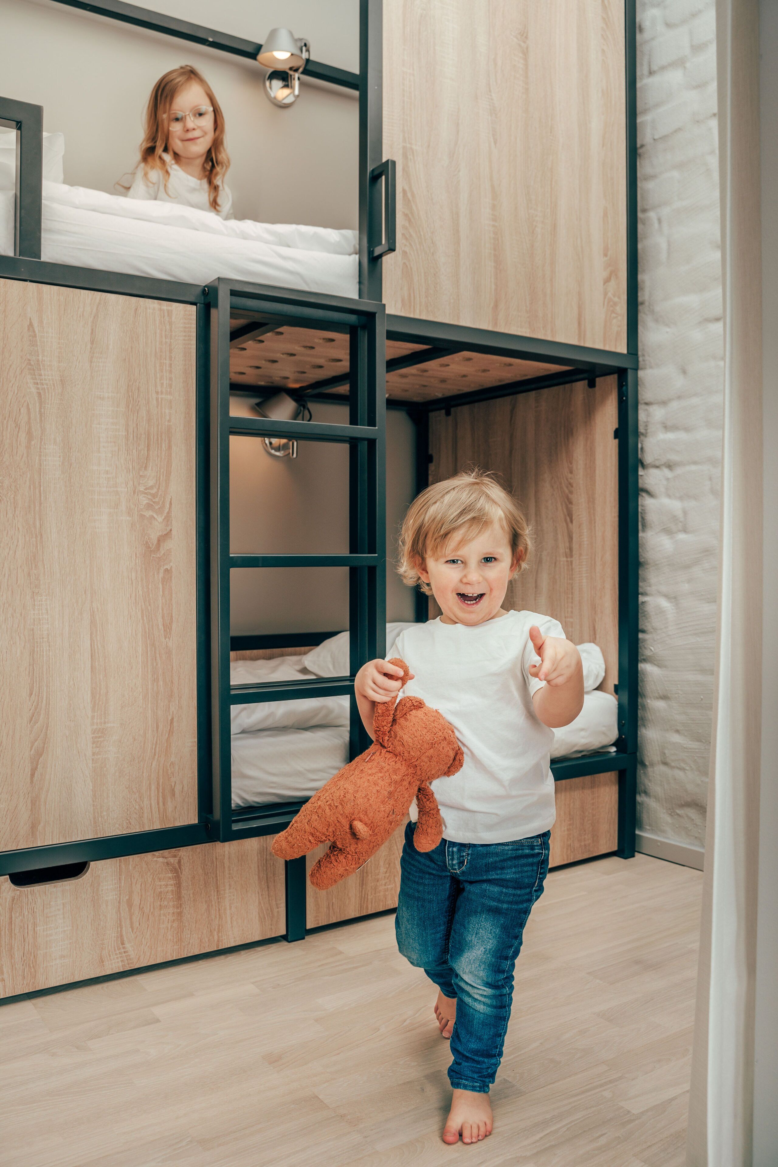 A child in a bunk bed room with wooden walls and a white mattress.