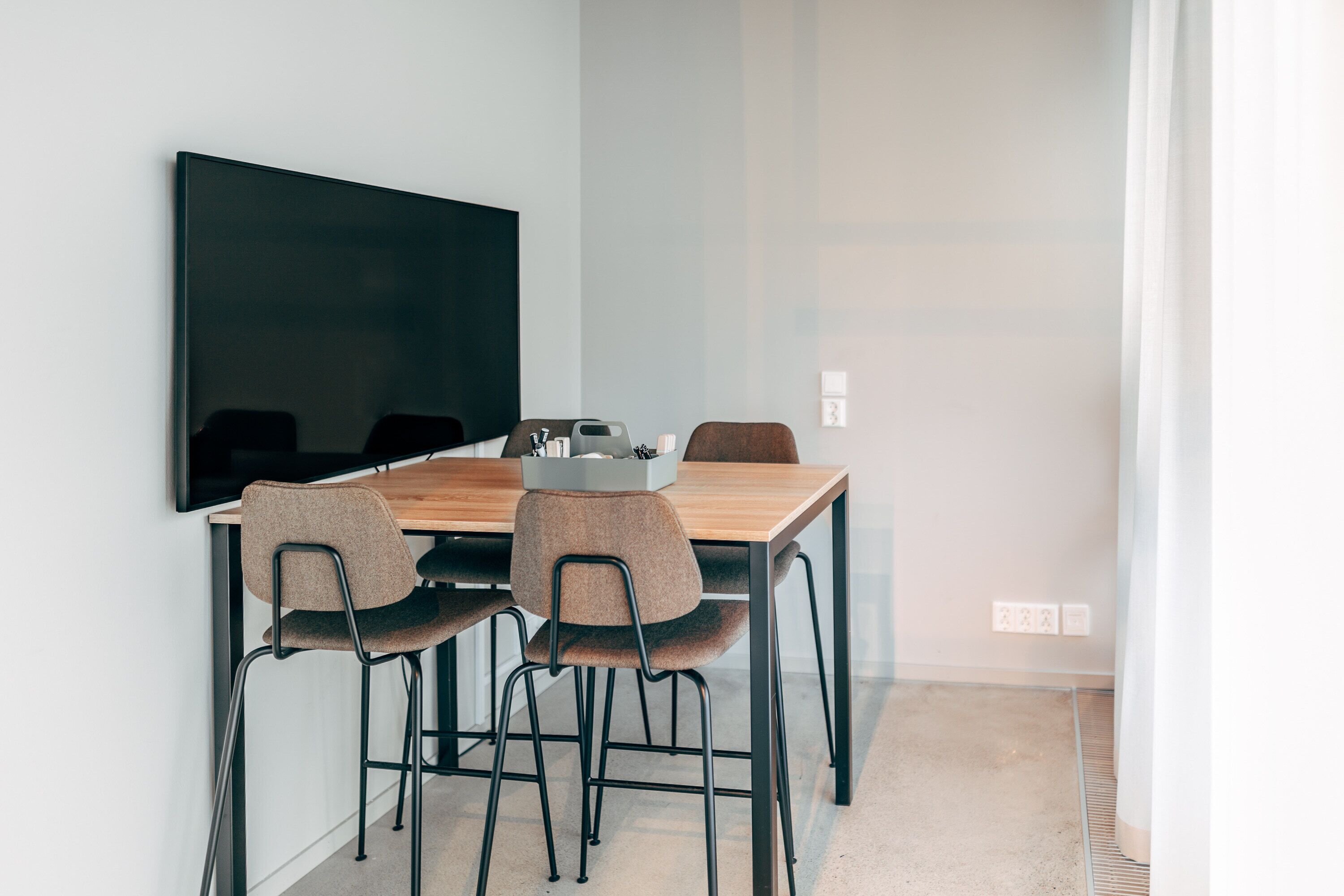 Un espace repas moderne avec une table en bois, quatre chaises et un téléviseur à écran plat fixé au mur.