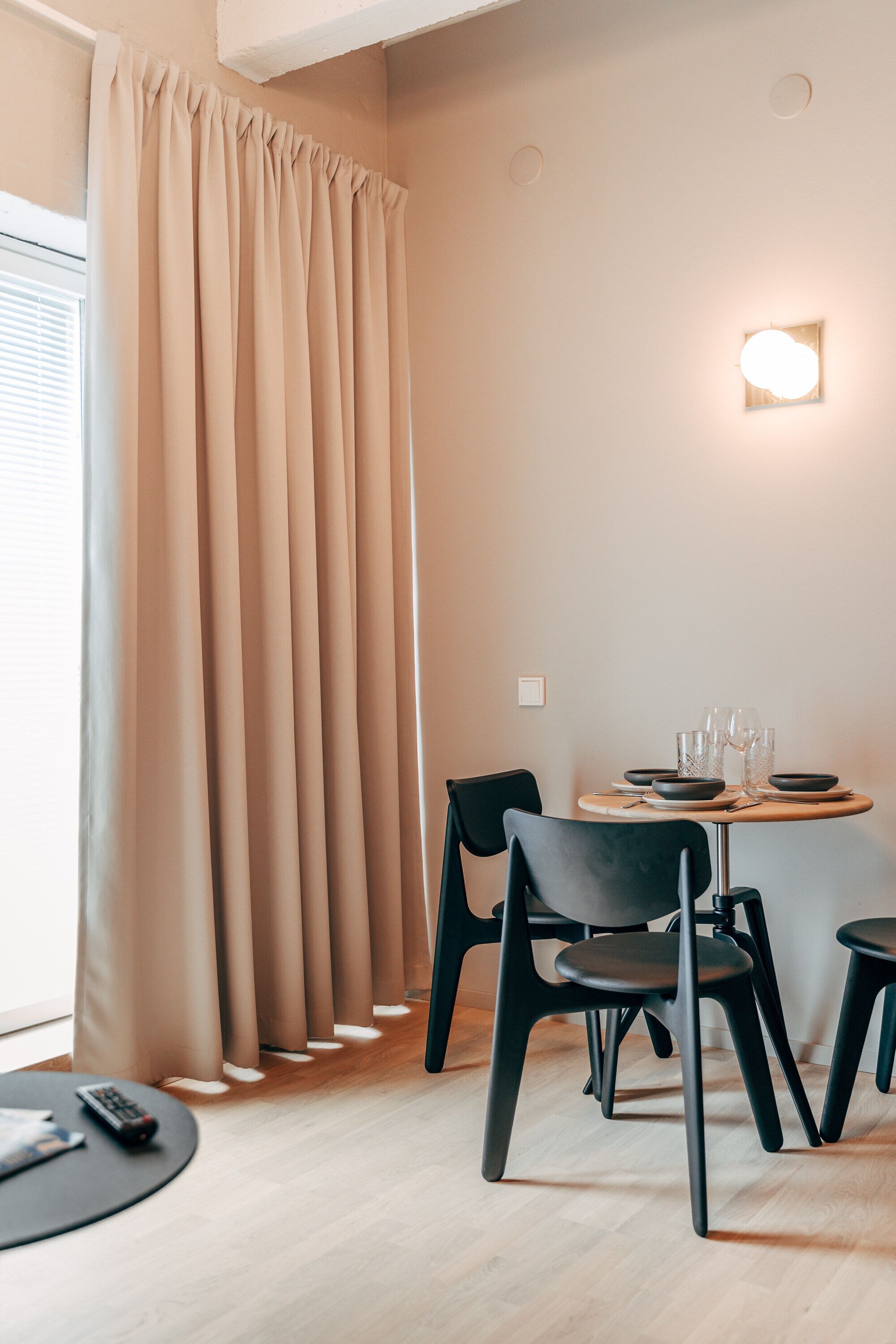 A modern dining area with a round table, black chairs, and a light fixture on the wall.