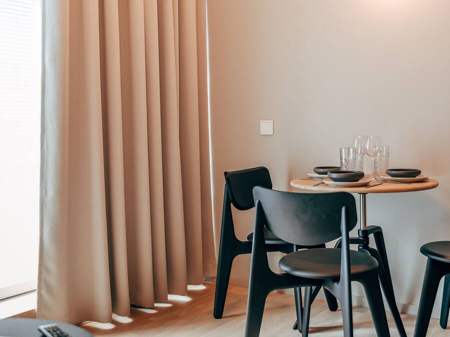A modern dining area with a round table, black chairs, and a light fixture on the wall.