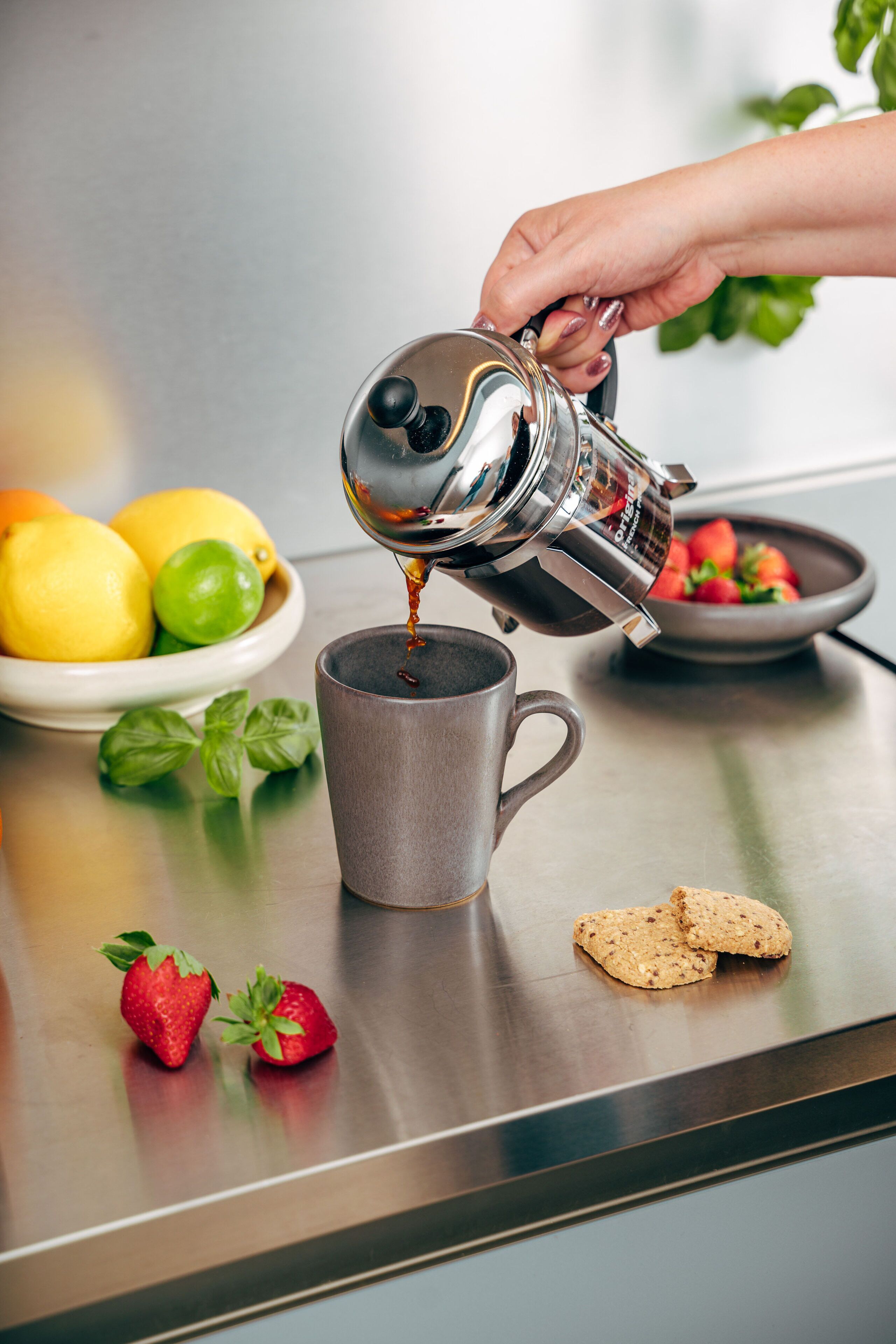 A hand pouring coffee into a mug on a stainless steel table.