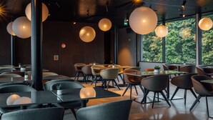 A modern dining area with round tables and chairs, large paper lanterns, and a view of trees through large windows. - Unity Tampere - A Studio Hotel (Tampere)