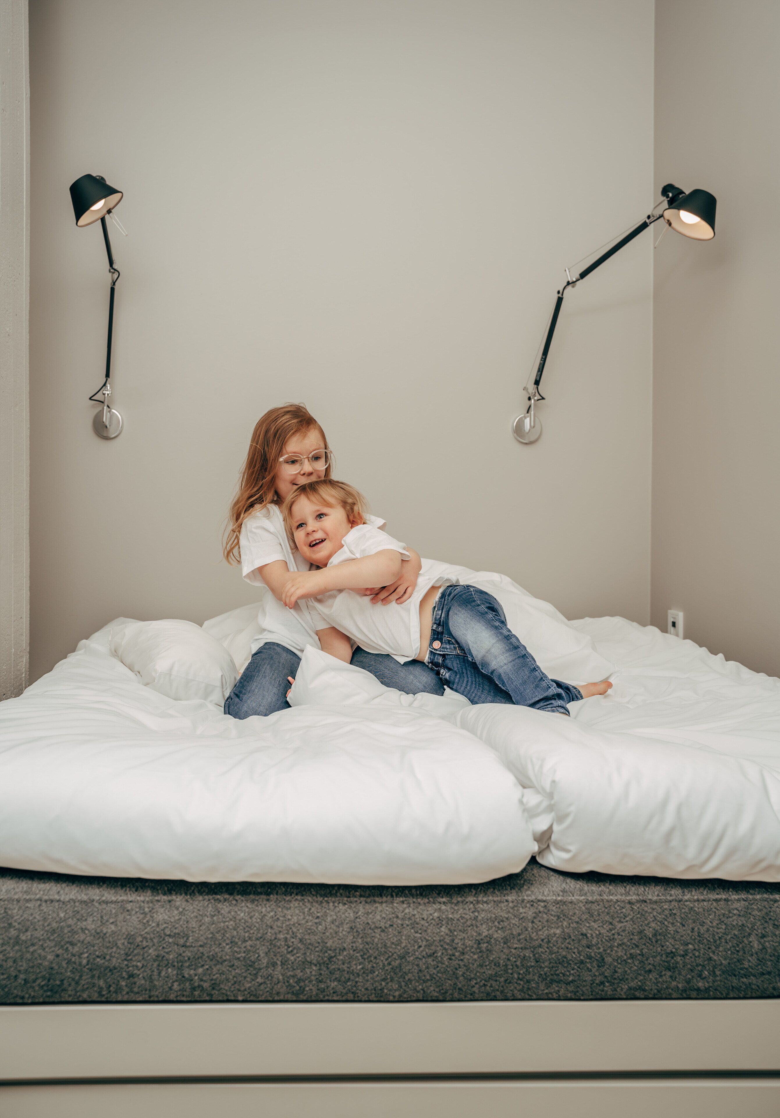 Een bed met witte beddengoed en twee zwarte vloerlampen aan weerszijden.